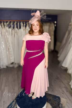 Plus size model in berry and blush off-the-shoulder occasion dress with rose detail and pleated panel by Veni Infantino, Curvy Chic Boutique Belfast