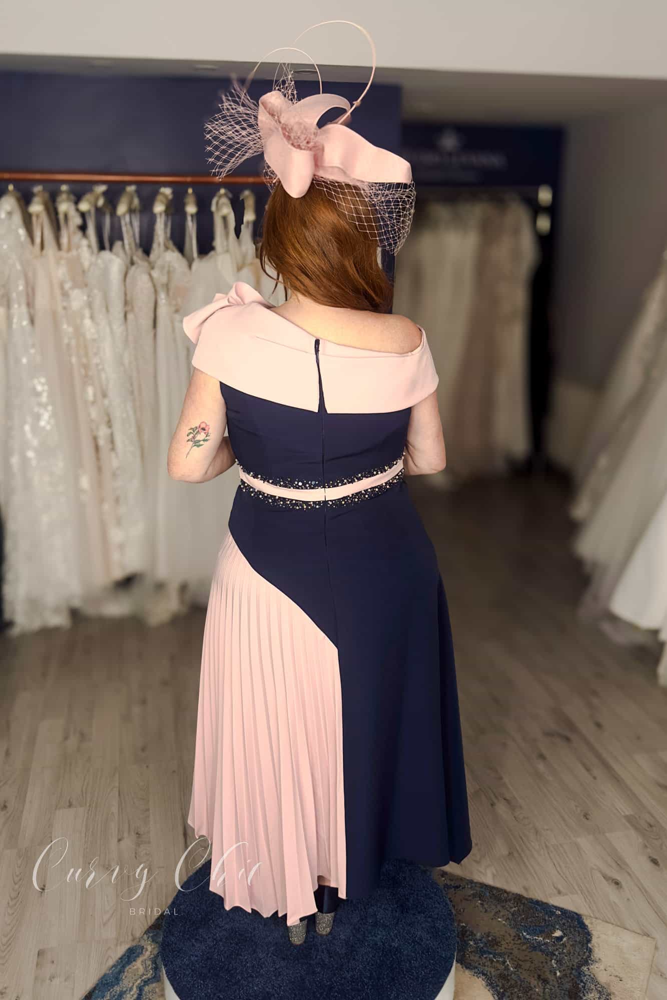 Plus size model wearing navy and blush asymmetric occasion dress with pleated skirt, back view, Curvy Chic Boutique Belfast